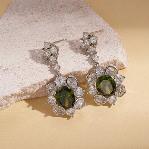 Detailed shot of flower earrings with oval green zircon and white crystals on stone base