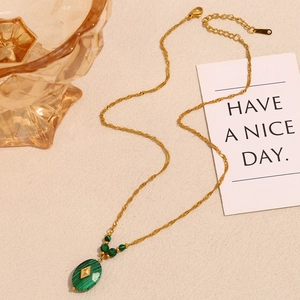 Detail of 18K gold-plated necklace with green malachite oval pendant on beige texture
