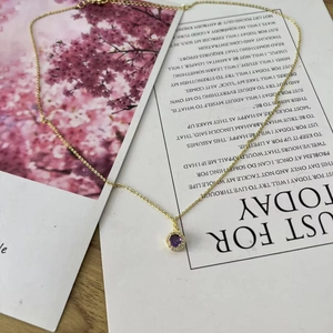 Detail of gold necklace with a round purple gemstone pendant and white diamond halo