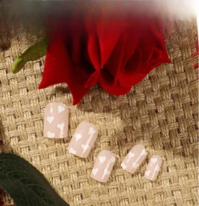 Detail of pink press-on nails with white heart patterns and red roses on burlap