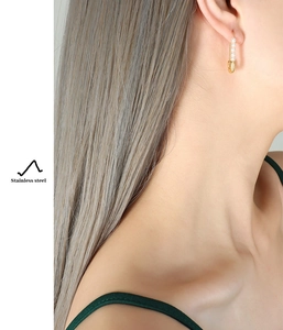 Close-up of gold paperclip earrings with white pearls on a model in stainless steel