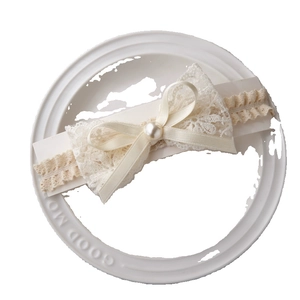 Bandeau bébé en dentelle avec nœud satiné et perle sur présentoir blanc épuré