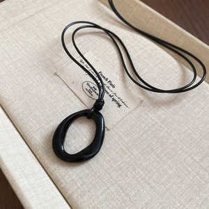 Vue macro du pendentif ovale noir asymétrique sur un support en tissu beige