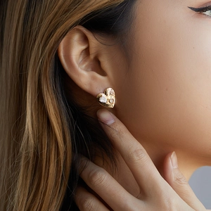 Close-up of heart-shaped gold earring with star engraving and teardrop zircon on model