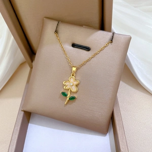 Close-up of a titanium steel gold flower necklace with white shell petals and green leaves