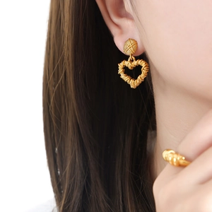 Golden heart-shaped woven texture earrings and ring set worn by model in a close-up view