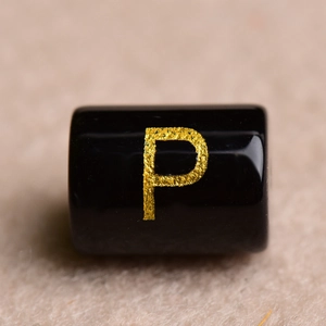 Macro shot of a black cylindrical bead with a golden letter P for DIY jewelry making