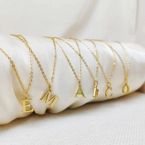 Detail of six minimalist golden letter pendants E M A I C O on white silk cylinders