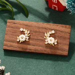 Macro shot of gold leaf earrings with white flowers and zircons on a wooden display