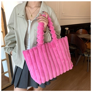 Close-up of bright pink plush tote bag with striped texture and fuzzy ball handle detail