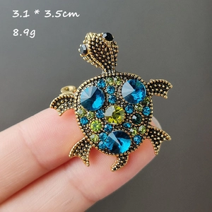 Detail of cartoon turtle brooch with blue rhinestones held to show 3.1 x 3.5cm size