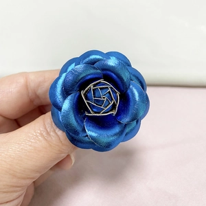 Close-up of blue metallic leather camellia brooch with golden geometric center