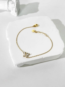Close-up of golden butterfly bracelet with marquise-cut zircons on a white stone tray