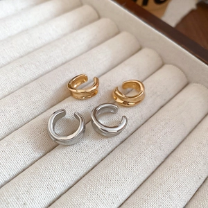 Set of minimalist gold and silver C-shaped ear cuffs on a beige jewelry display tray
