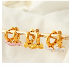 Detail of gold earrings with pink, yellow and white heart-shaped crystals on white silk