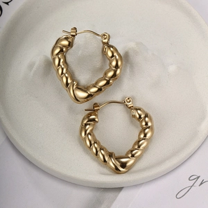Macro detail of gold-plated heart-shaped twisted hoop earrings on a ceramic display