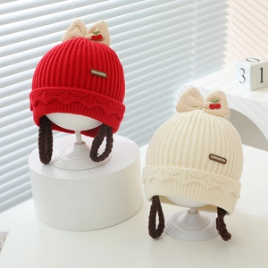Détail du bonnet tricoté pour bébé avec décorations cerises et tresses intégrées