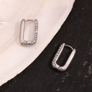 Detailed macro view of silver U-shaped earrings with pavé zircons on marble background