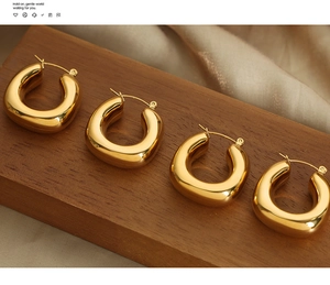 Macro shot of two pairs of thick U-shaped gold-plated hoop earrings on a dark wood base