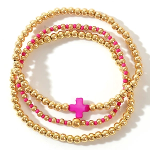Three-layer gold beaded bracelet set with pink beads and a shell cross pendant