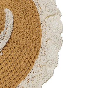 Close-up of beige woven straw hat featuring delicate white floral lace trim detailing