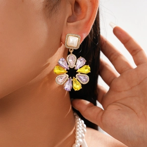Detail of flower-shaped earrings with purple gems, yellow stones and sparkling rhinestones