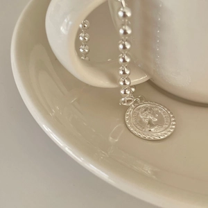 Detail of silver bead chain bracelet with a vintage coin pendant on a ceramic cup