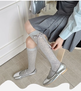 Detail of grey knitted knee-high socks with silk ribbon bows and Mary Jane shoes