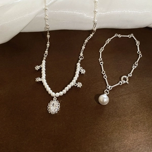 Detailed set of silver zircon flower pendant necklace and pearl bracelet on silk fabric