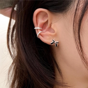 Close-up of black bow stud earring and silver pave ear cuffs worn by a female model