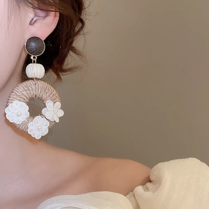 Close-up of bohemian rattan hoop earrings with white fabric flowers and pearl accents