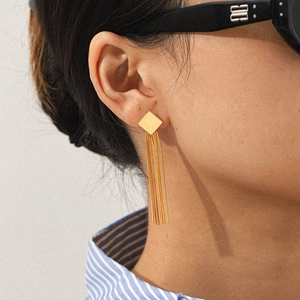 Model wearing gold long fringe earrings with geometric square stud in a high-end style