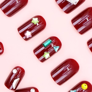 Macro shot of deep red glossy press-on nails with colorful rhinestones in star shapes