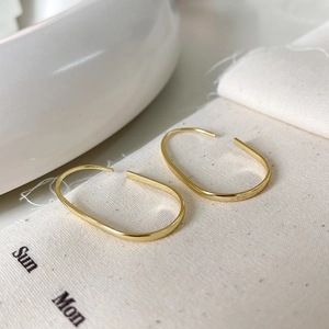 Detailed view of gold U-shaped silver earrings on textured fabric and ceramic props