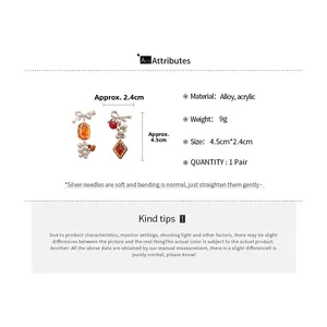 Detail view of asymmetric bow earrings with orange acrylic beads and size measurements