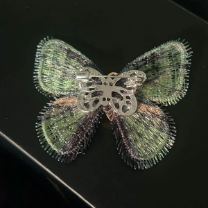 Detailed back view of green and purple butterfly brooch with silver metal pin fastening