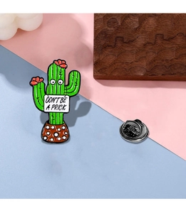 Detail of green cactus enamel pin with 'DON'T BE A PRICK' text on colorful backdrop
