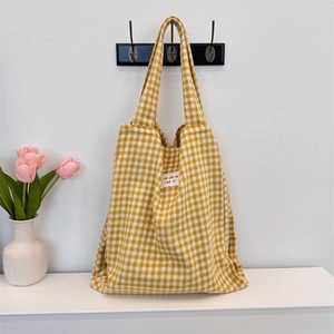 Detail of yellow plaid tote bag hanging on a hook with floral decor in a cozy setting