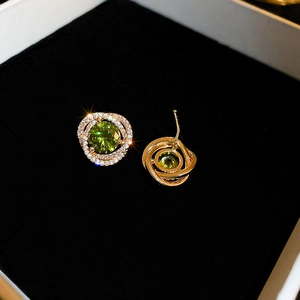 Macro shot of gold spiral earrings featuring a central green gemstone and micro diamonds