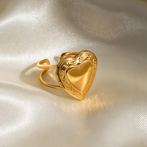 Vintage gold heart locket ring with embossed pattern on elegant white satin background