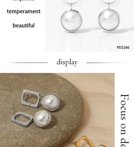 Detail of square silver steel pearl earrings displayed on a white and stone background