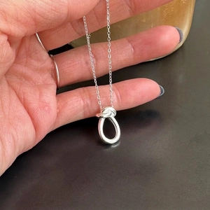 Handheld view of a 925 sterling silver knotted pendant necklace with fine link chain