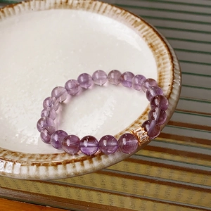 Macro detail of purple crystal beaded bracelet with gold inlaid charm in a ceramic dish