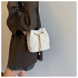 Detail of white bucket bag with fringe texture, golden chain, and pearl drawstring