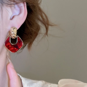 Close-up of a model wearing gold hammered metal and red acrylic geometric drop earrings