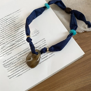 Detail of dark blue fabric necklace with translucent resin pendant on vintage book pages