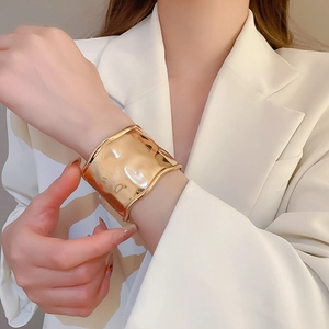 Close-up of wide gold cuff bracelet featuring wavy texture on a model's wrist