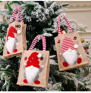 Close-up of festive burlap Christmas gift bags with 3D gnome designs on snowy tree