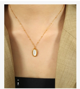 Detail of gold oval white shell pendant necklace with small beads on an elegant model