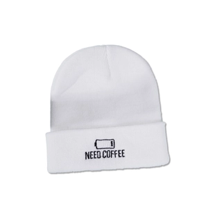 Close-up of white knit beanie featuring black NEED COFFEE embroidery and battery icon